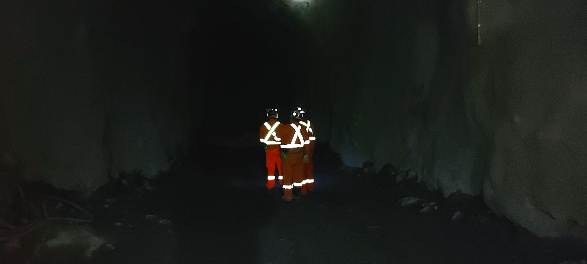 Two crew members walking back through a mine drift, backlit
