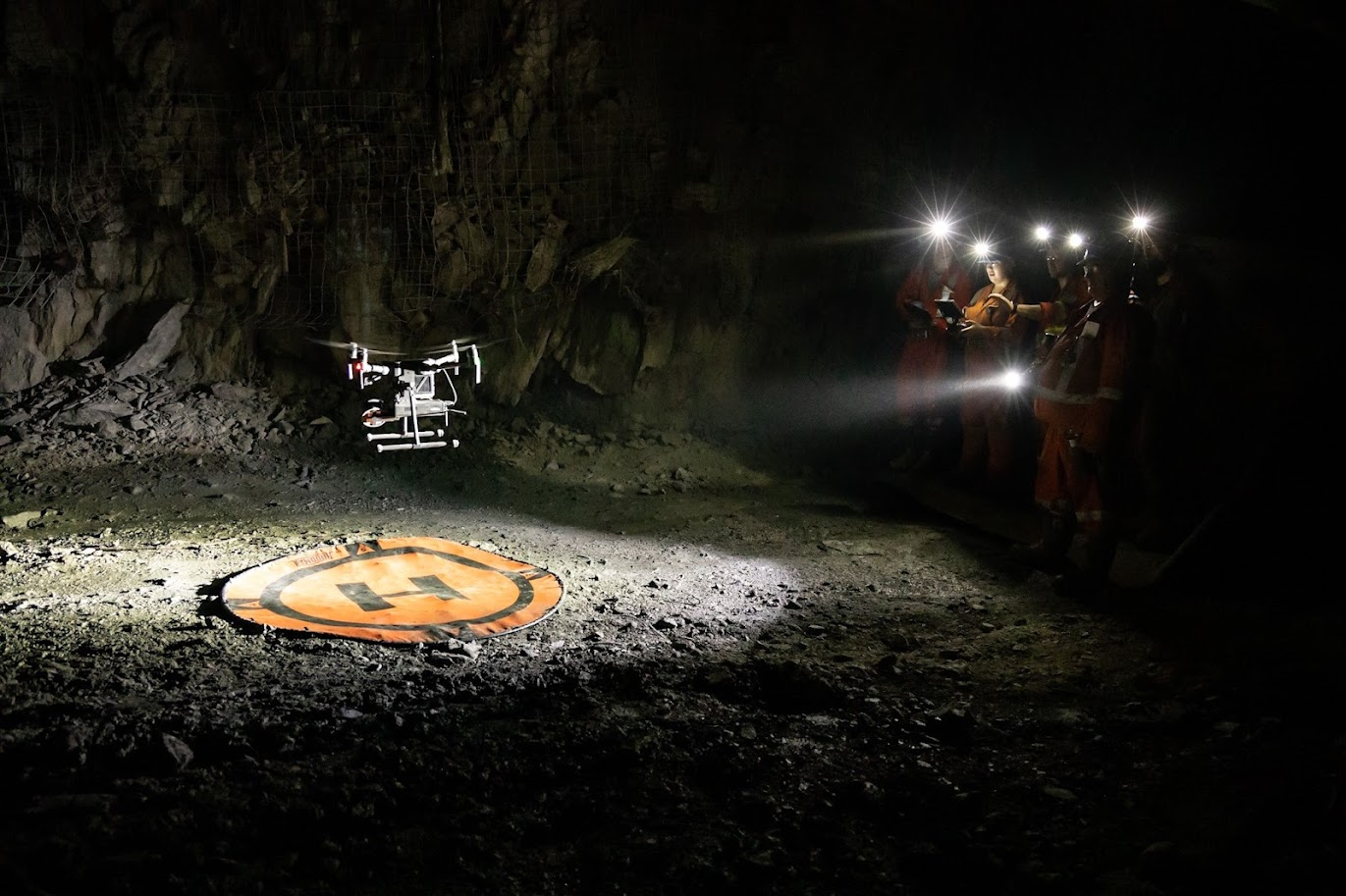 Crew of four with headlamps watching a drone land on a pad underground